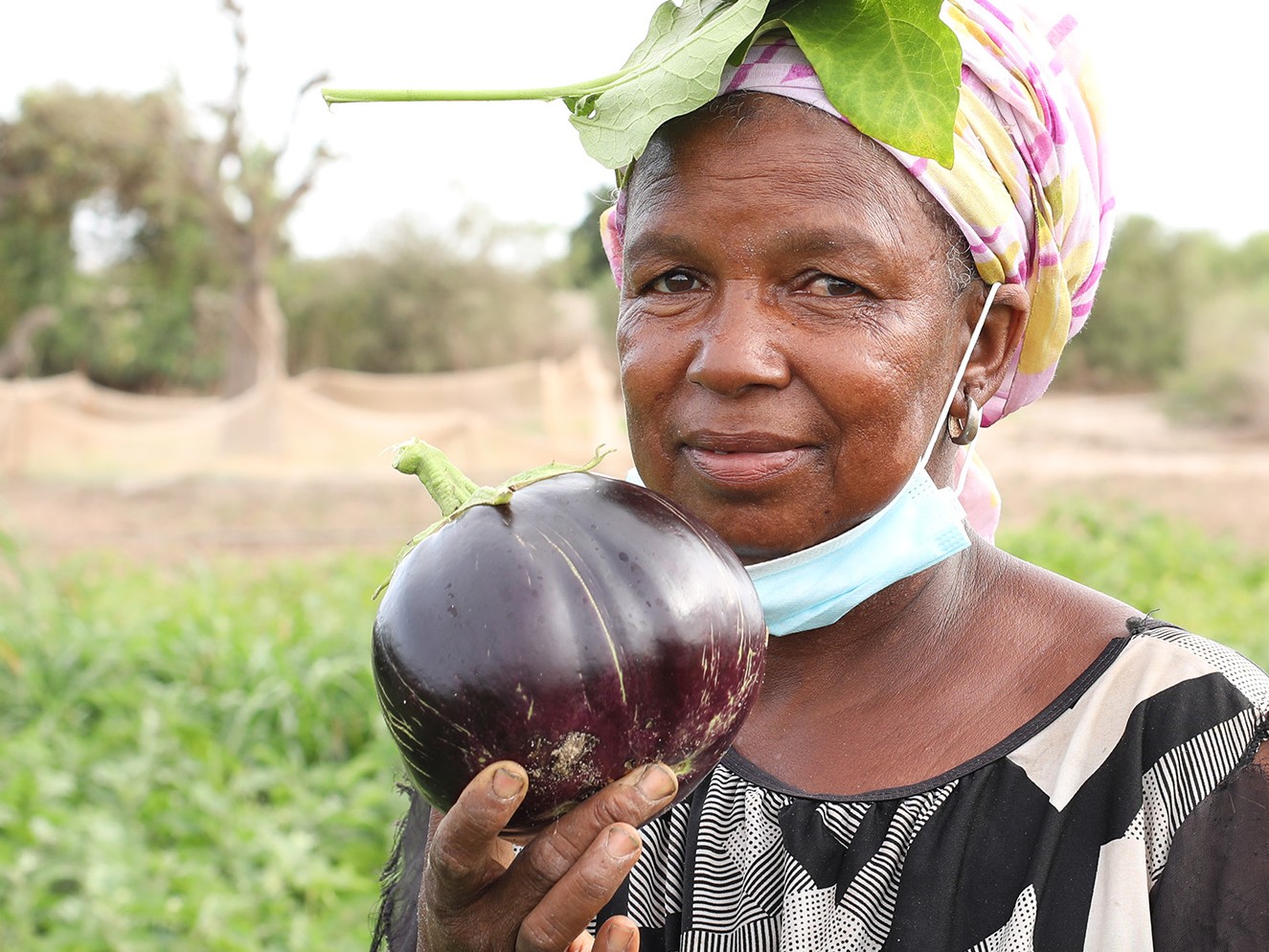 A woman in a black and white shirt holds an eggplant