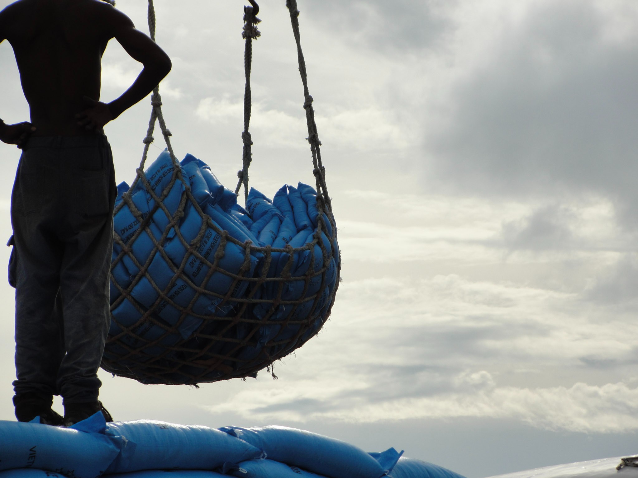 A man stands on fertilizer bags while a crane moves several in front of him