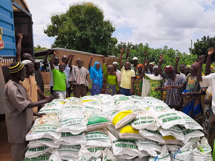African farmers stand around bags of fertilizer or seed